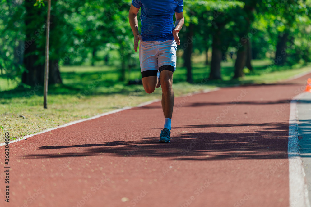 Photo of running shoes and strong athletic legs of sport man jogging on the running track Photo of running shoes and strong athletic legs of sport man jogging on the running track