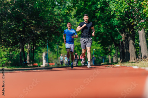 Two healthy young men running in the park on a sunny day.. © qunica.com