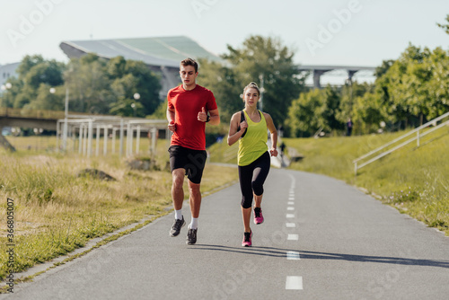Full-length front view of an attractive caucasian couple running together in a park on a sunny day.. © qunica.com