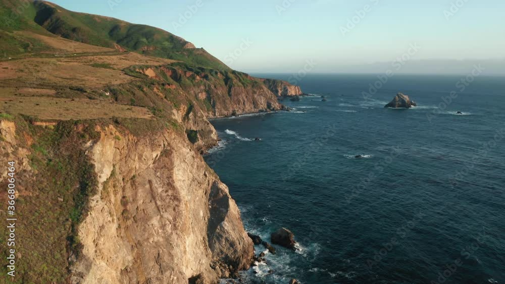 4K cinematic aerial view of golden sunset light covering the scenic rocky coast and beautiful deep blue Pacific ocean, with waves crashing on the picturesque sea rocks, USA. summer travel background 4K cinematic aerial view of golden sunset light covering the scenic rocky coast and beautiful deep blue Pacific ocean, with waves crashing on the picturesque sea rocks, USA. summer travel background