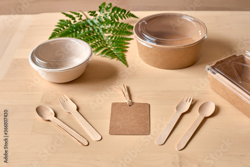 Recyclable carton food package and wooden fork and knife placed on table with fern leaf photo