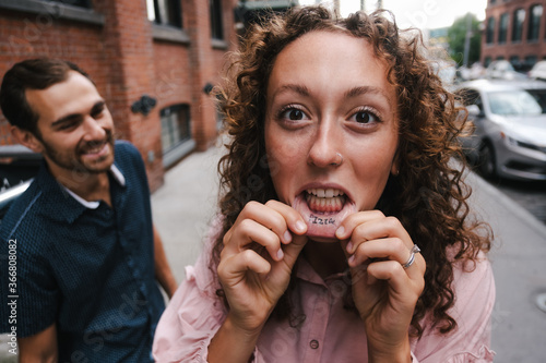 Cheerful female with curly hair showing tattoo on lips during city walk with boyfriend in New York photo