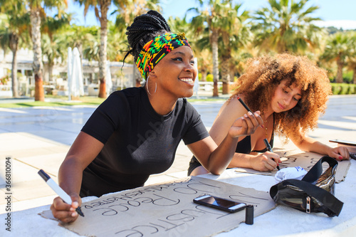 Diverse female activists making placards with black lives matter and no justice no peace inscriptions while preparing for strike against racism