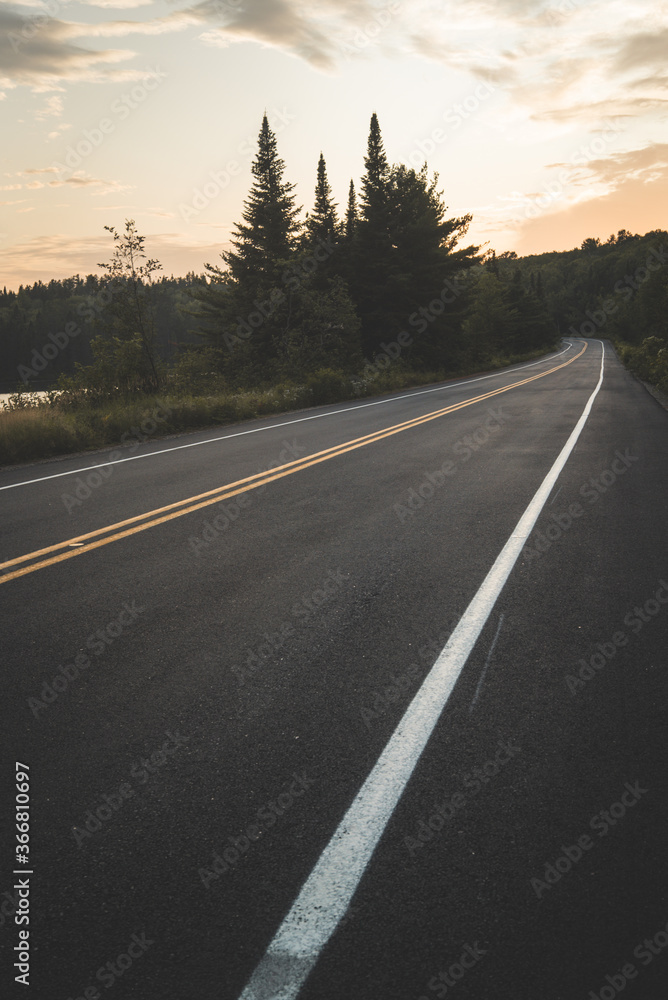 Asphalt road going near peaceful lake and green forest against cloudy sunset sky in La Mauricie National Park in Quebec, Canada Asphalt road going near peaceful lake and green forest against cloudy sunset sky in La Mauricie National Park in Quebec, Canada