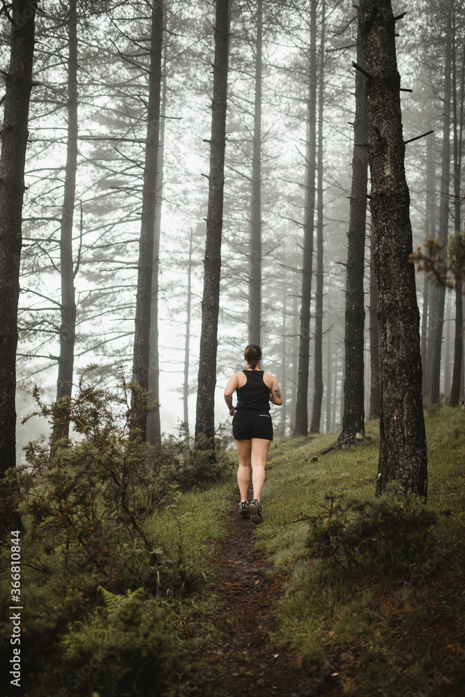 Fit woman running along path in misty forest Fit woman running along path in misty forest