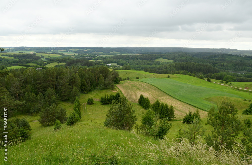 View from a tall mountain with some trees, fields, meadows, and forest visible below spotted on a cloudy yet warm summer day on a Polish countryside during a hike