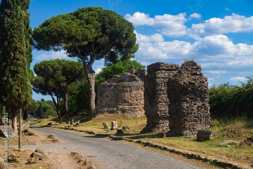 Circular tomb and funeral monuments on the Appia Antica, Rome, on a sunny day. It was one of the most important roads of the Roman Empire, remains of the pavement, maritime pines, cypresses