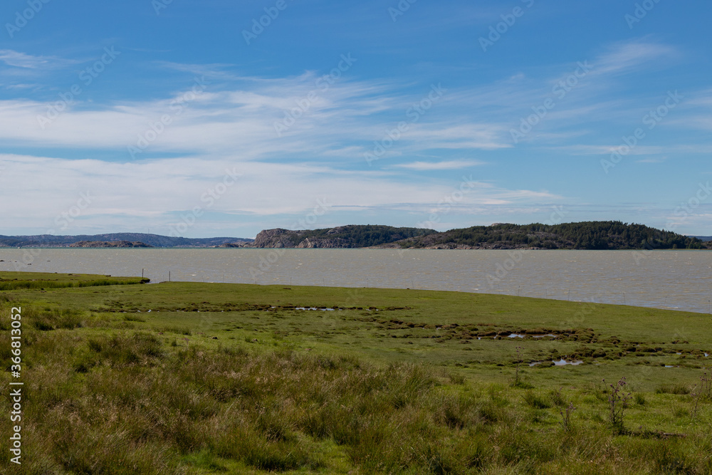A grassy part of the coastline in the Swedish archipelago.
There is a blue sky and islands in the background A grassy part of the coastline in the Swedish archipelago.
There is a blue sky and islands in the background