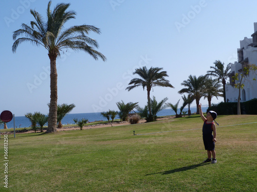 Little child on a green lawn with palm trees near the sea