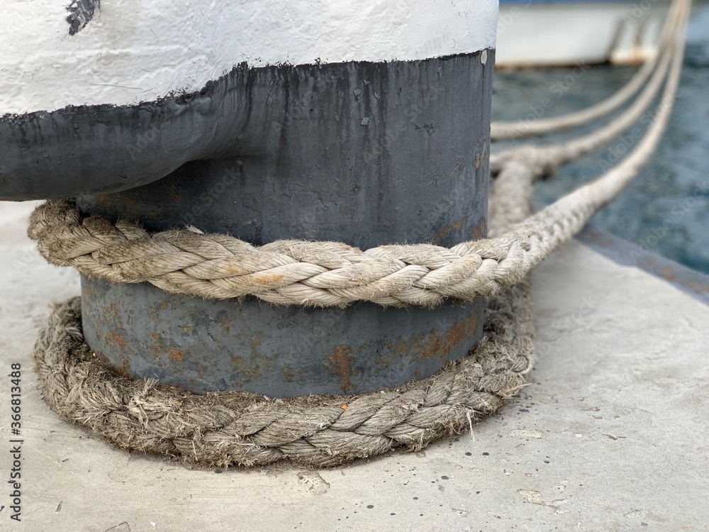 Fototapeta premium The ship's rope is tied to a post in the dock. The ship is moored to the shore. The rope keeps the boat on the pier.