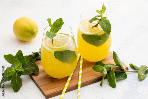 Lemon lemonade with ice and mint on a wooden board on a white-gray background.