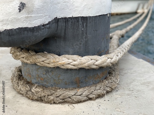 The ship's rope is tied to a post in the dock. The ship is moored to the shore. The rope keeps the boat on the pier.
