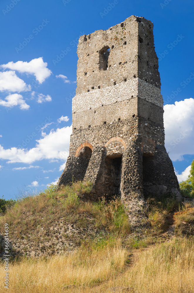 The imposing structure of the funerary monument called Torre Selce in brick on the Via Appia Antica, Rome, Italy. Photographed on a summer day with sun and clouds surrounded by a yellow meadow.