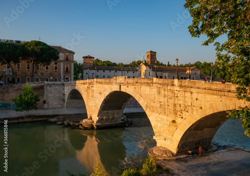 View of the Ponte Fabricio Rome, which connects the Tiber island to the Jewish quarter. The bridge reflects with shadows its arches in the Tevere river at sunset on a hot summer day.
