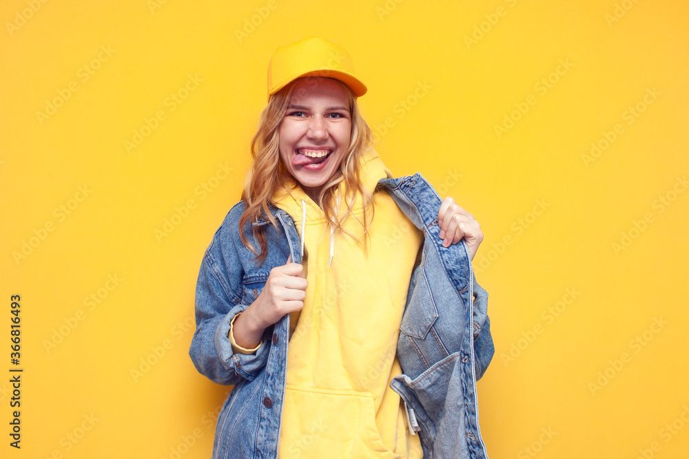 crazy girl in denim jacket and cap posing on yellow isolated background, funny hipster girl smiling and showing tongue, copy space crazy girl in denim jacket and cap posing on yellow isolated background, funny hipster girl smiling and showing tongue, copy space