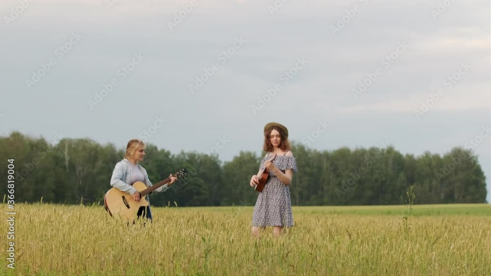 two young beautiful women play country music on guitar and ukulele. Wheat field at sunset on a summer evening two young beautiful women play country music on guitar and ukulele. Wheat field at sunset on a summer evening