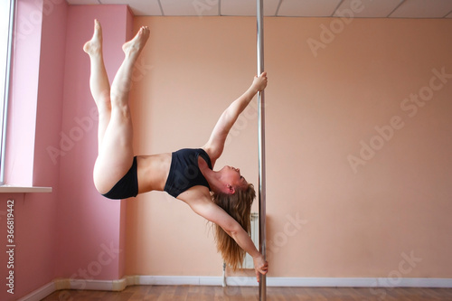 pole dance training, athletic girl does exercise on a pylon, gymnast does a difficult trick
