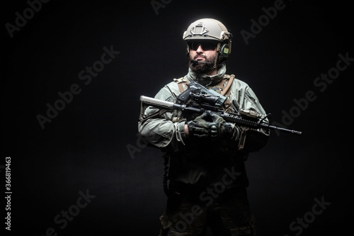 American special forces against a dark background, a soldier in military equipment holds weapons and looks at the copy space, elite troops