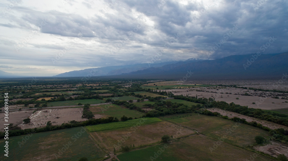 Rural landscape at sunset. Aerial view of the alfalfa and crop plantation fields and farmland in the mountains, under a dramatic sky with beautiful clouds. Rural landscape at sunset. Aerial view of the alfalfa and crop plantation fields and farmland in the mountains, under a dramatic sky with beautiful clouds.