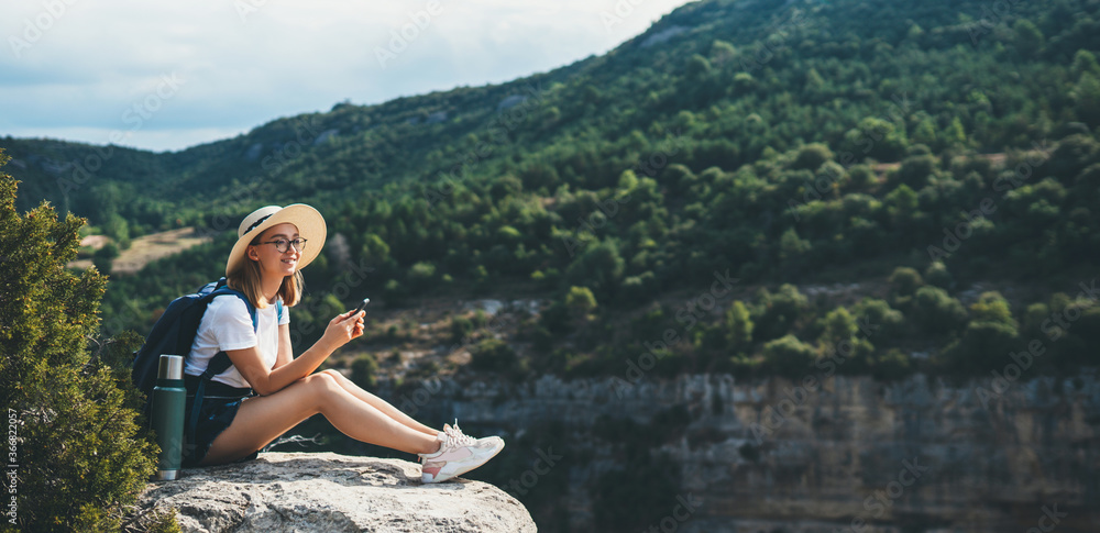 hipster traveler in hat and backpack ralaxing in nature and plans route online map in smartphone, tourist girl uses cellphone on background of panorama horizon mountain landscape empty space hipster traveler in hat and backpack ralaxing in nature and plans route online map in smartphone, tourist girl uses cellphone on background of panorama horizon mountain landscape empty space