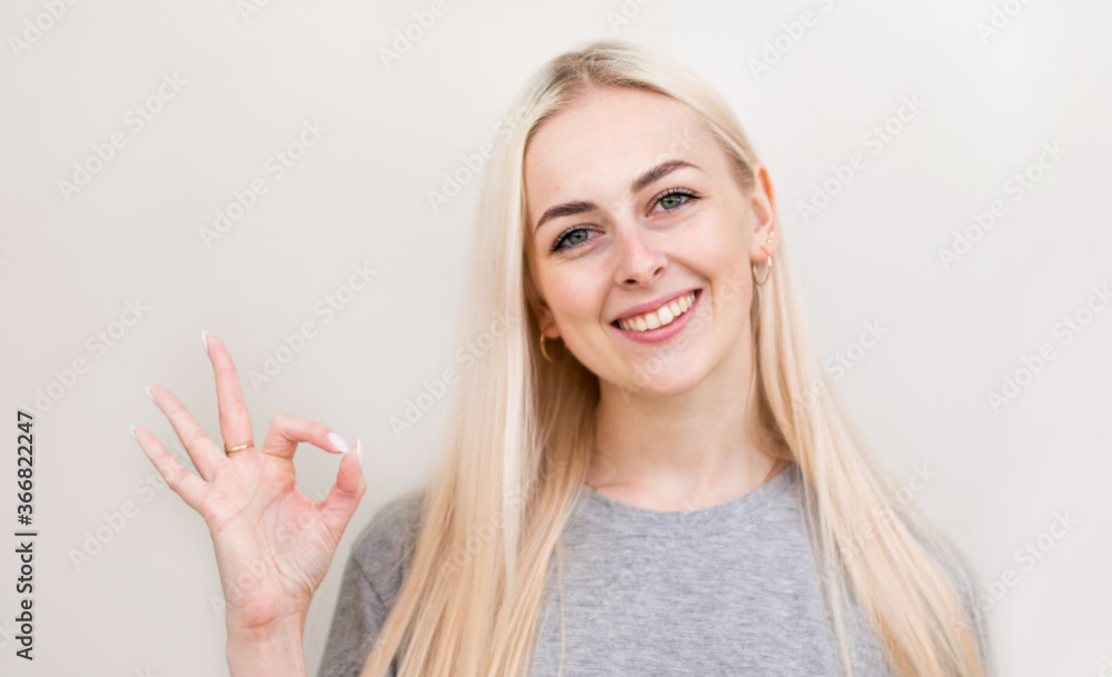 Young lighthearted girl shows okay gesture, isolated on beige Young lighthearted girl shows okay gesture, isolated on beige