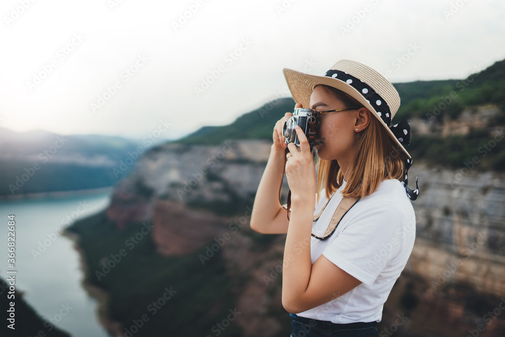 activ young blonde girl in summer hat takes photo on retro camera of panorama horizin mountain landscape walking on trip outdoors, hipster tourist enjoys hobby of photographing nature spain on holiday