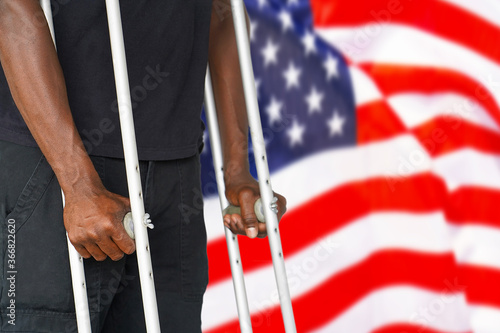 African man on crutches on the background of the USA flag. Disabled veterans of the US Army. The concept of violence and racism in USA photo