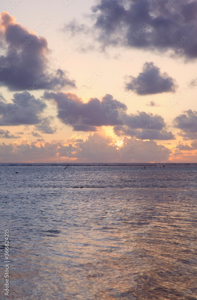 Sun sinks to Sea under a cloud-filled Sky at Sunset