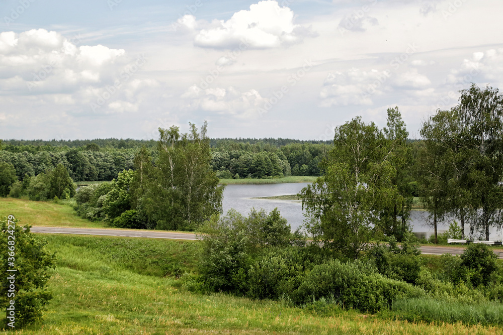 Summer landscape with field, river, road and cloudy sky