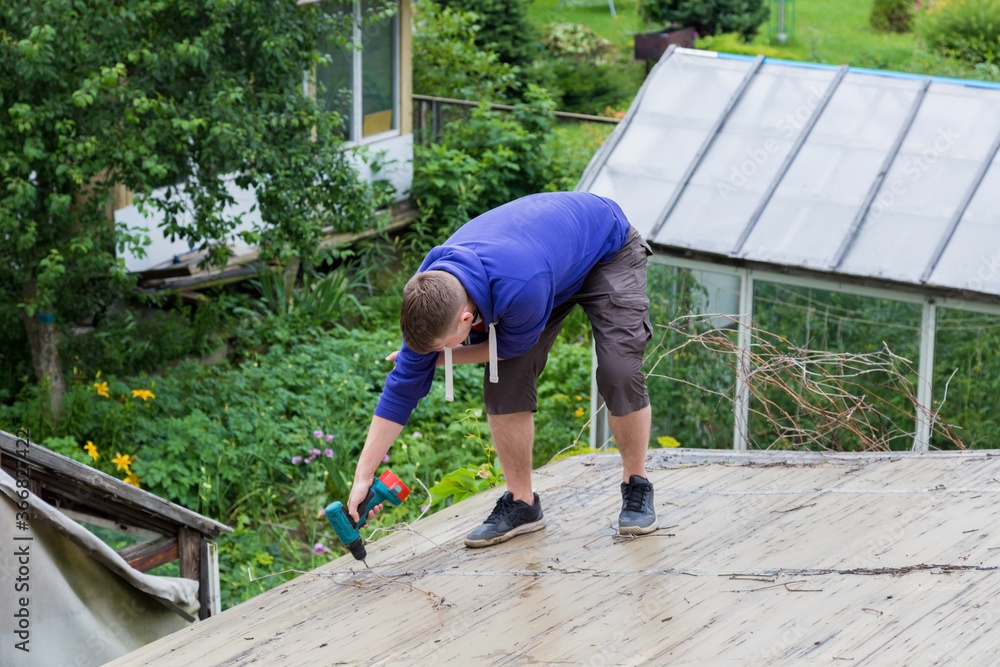 A man holds a screwdriver in his hands while standing on the roof A man holds a screwdriver in his hands while standing on the roof