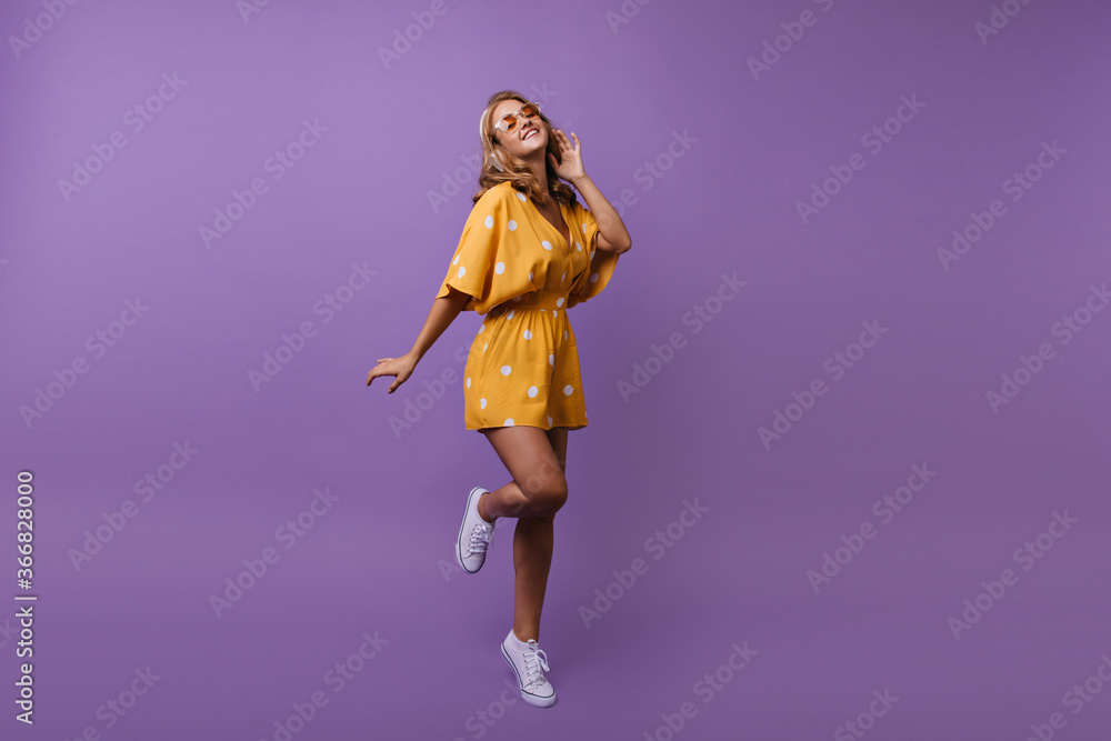 Full-length shot of blissful girl with curly hairstyle dancing and smiling. Studio portrait of refined shapely lady in yellow outfit. Full-length shot of blissful girl with curly hairstyle dancing and smiling. Studio portrait of refined shapely lady in yellow outfit.