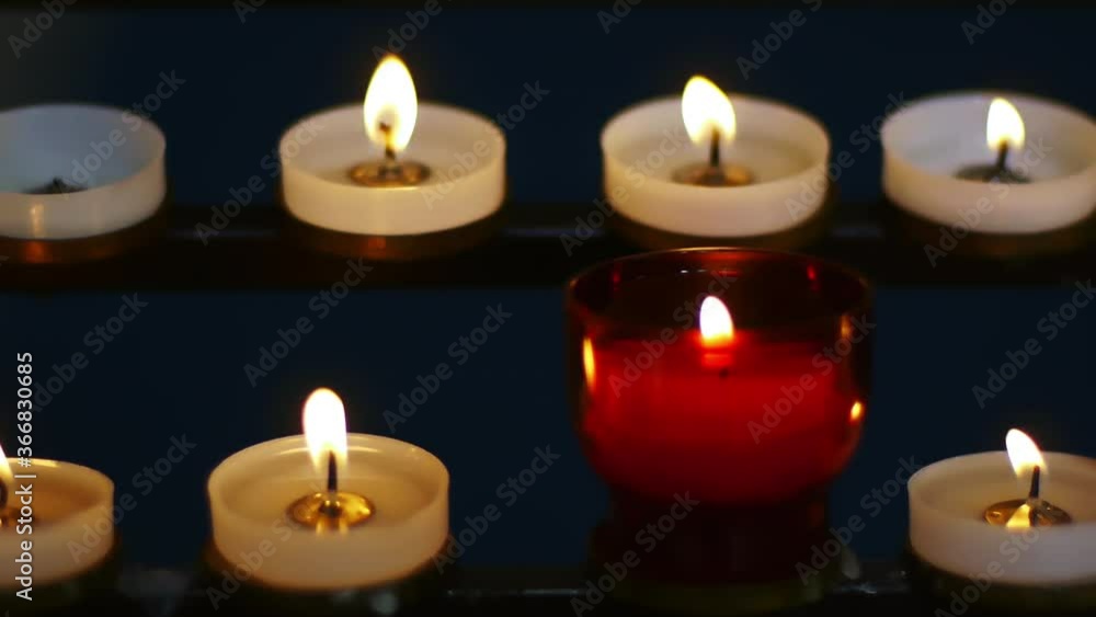 many small white and red church candles in a monastery church in UK. illuminated on black background in close up shoot many small white and red church candles in a monastery church in UK. illuminated on black background in close up shoot