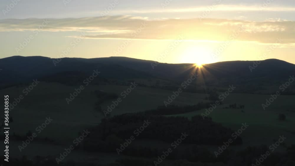 Static timelapse 4k shot of the sun rising from behind a mountainous horizon above a still countryside in Dolní Morava, Czech Republic covered with shadows. Summer countryside in Czechia at sunrise.