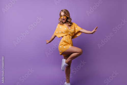 Graceful european girl dancing with surprised smile. Studio photo of magnificent blonde lady standing on one leg.