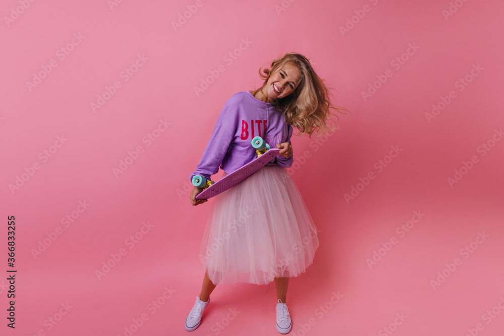 Full-length photo of joyful lady with blonde hair. Active stylish girl dancing with skateboard.