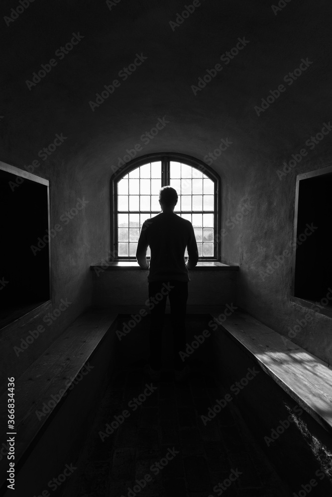 Rear view of young man looking through wooden vintage window with sunlight in black and white