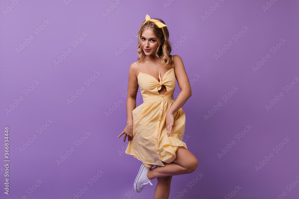Obraz premium Cheerful young woman playfully dancing on purple background. Pretty curly girl expressing good emotions during photoshoot.