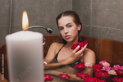 a young girl is sitting in a wooden tub filled with water with rose petals