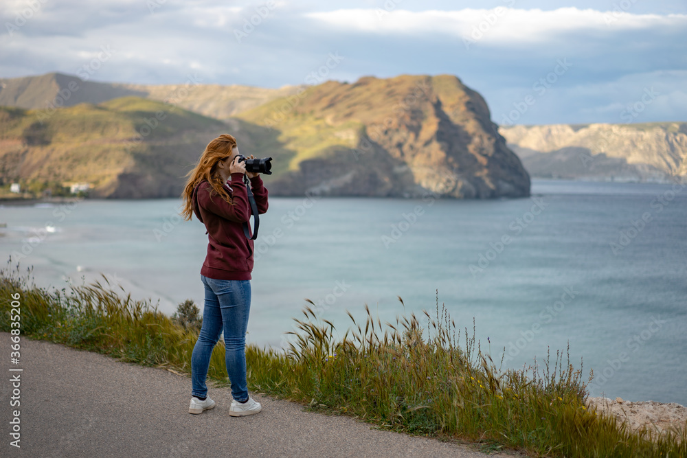 Side view of woman photographing seascape with camera while standing on mountain