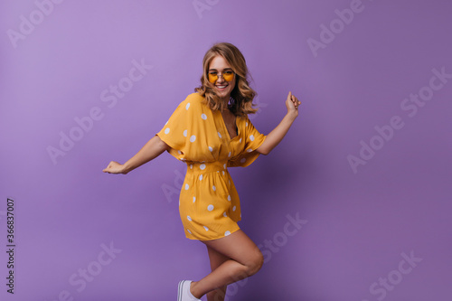 Ecstatic fair-haired girl with tanned skin dancing on purple background. Pleased lady with elegant wavy hairstyle fooling around in studio. © Look!
