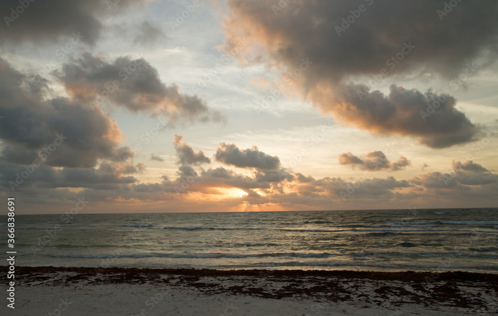 Magical seascape. The beach at sunset. The white sand, sargassum seaweed, coastline and sea waves. Beautiful twilight colors in the sky and sea water surface.