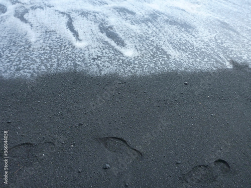 Foot prints on Punalu'u black sand beach on the Big Island of Hawaii as the surf rolls in
