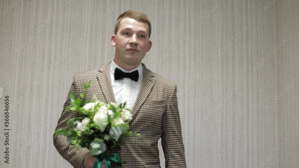 Groom with wedding bouquet in his hands at home. White shirt, jacket Groom with wedding bouquet in his hands at home. White shirt, jacket