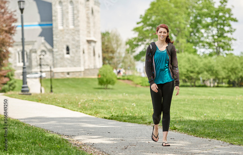 Beautiful female student, with red hair, wearing backpack on campus - walking down path