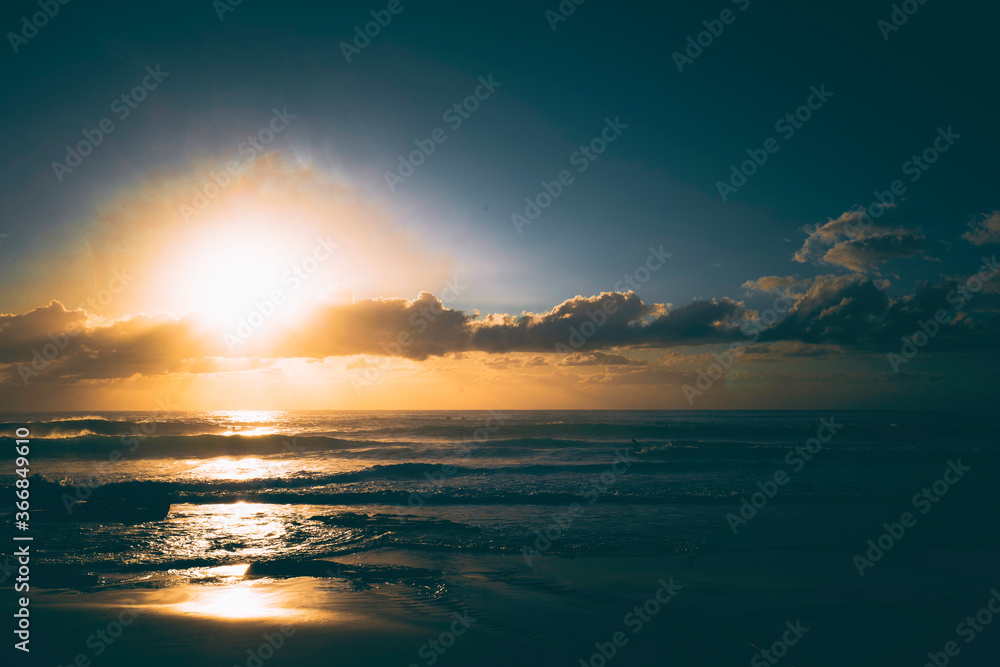 Sunrise over the ocean, with silhouette of surfer catching a wave
