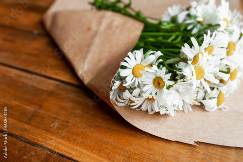 lush bouquet of small daisies in craft paper on wooden table