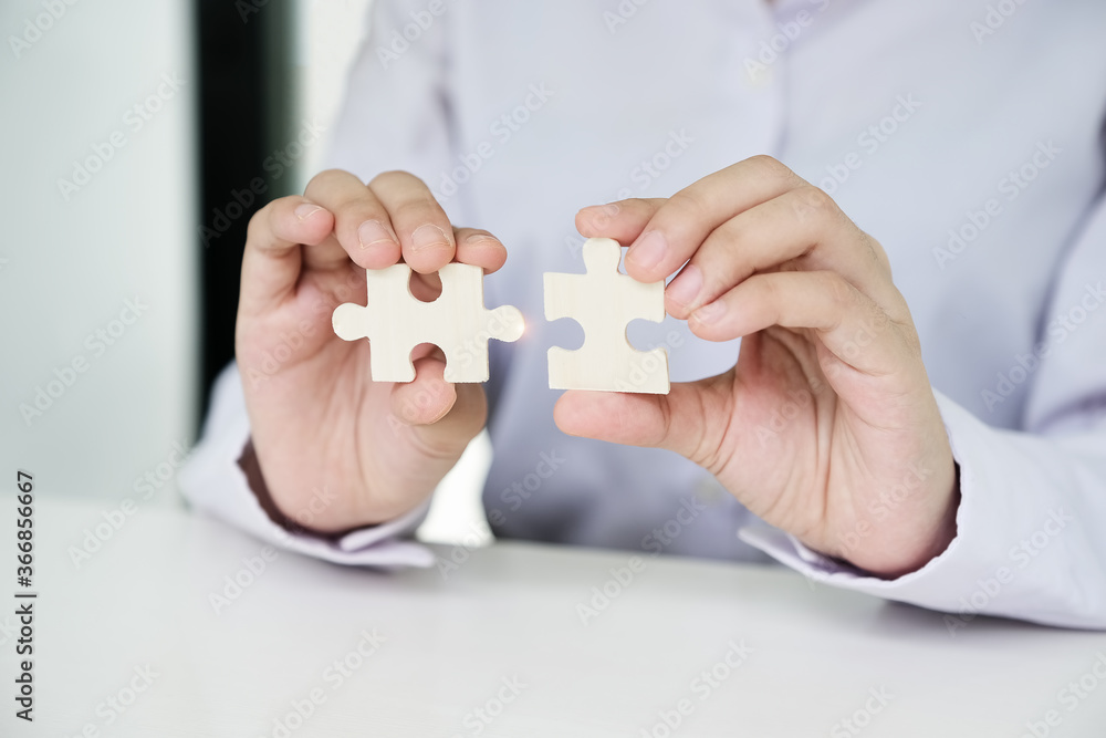 businesswomen using two hands trying to connect couple puzzle piece Jigsaw alone wooden puzzle against sun rays. one part of whole. symbol of association and connection. support and help concept. businesswomen using two hands trying to connect couple puzzle piece Jigsaw alone wooden puzzle against sun rays. one part of whole. symbol of association and connection. support and help concept.