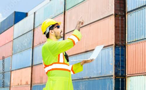 Engineers with hard hat talking by walkie talkie with team for working at the containers box in warehouse outdoors background.Engineer man assign from portable radio at business logistics site.