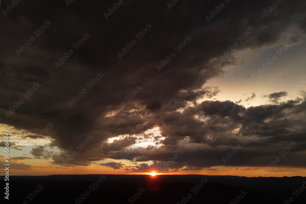 bright orange sunset with storm clouds and silhouette of mountains with red sun