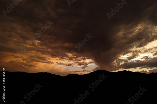 bright orange sunset with storm clouds and silhouette of mountains